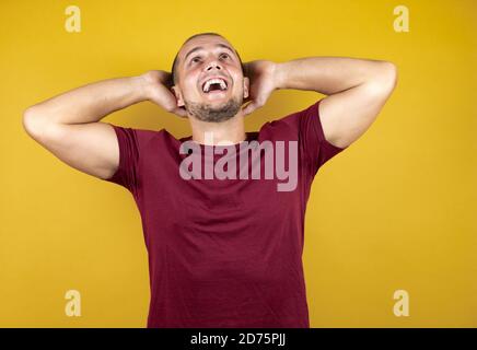 Russian man wearing basic red t-shirt over yellow insolated background relaxing and stretching, arms and hands behind head and neck smiling happy Stock Photo