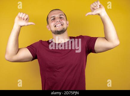 Russian man wearing basic red t-shirt over yellow insolated background looking confident with smile on face, pointing oneself with fingers proud and h Stock Photo