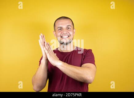 Russian man wearing basic red t-shirt over yellow insolated background clapping and applauding happy and joyful, smiling proud hands together Stock Photo