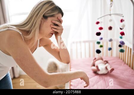 mother suffering from postnatal depression near crib with cute baby at home Stock Photo