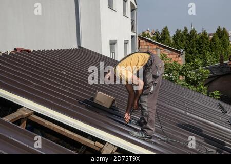 Repairing the roof of the house with screws drive tools. Worker roofer builder working on roof structure Stock Photo