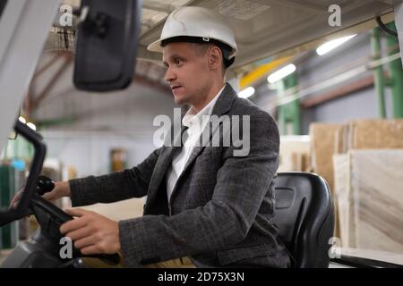 Concentrated worker of storehouse sitting in lift truck and looking forward while loading materials Stock Photo