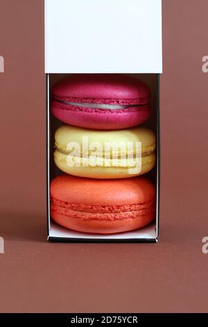 Multicolored macarons in a cardboard box with an open lid standing upright on a brown background. Closeup Stock Photo