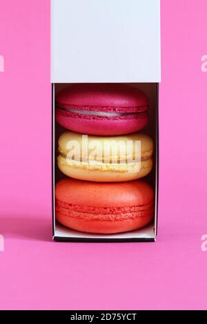 Multicolored macarons in a cardboard box with an open lid standing upright on a pink background. Closeup Stock Photo