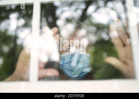 An elderly woman in a protective mask in front of window look outside Stock Photo