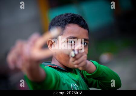 Bangladesh – October 04, 2020: A Bangladesh cricket jersey-wearing kid boy shooting a wooden slingshot at Barinagar, Jessore. Stock Photo