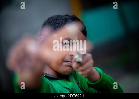 Bangladesh – October 04, 2020: A Bangladesh cricket jersey-wearing kid boy shooting a wooden slingshot at Barinagar, Jessore. Stock Photo