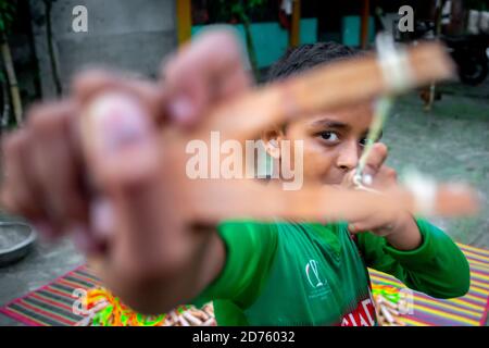 Bangladesh – October 04, 2020: A Bangladesh cricket jersey-wearing kid boy shooting a wooden slingshot at Barinagar, Jessore. Stock Photo