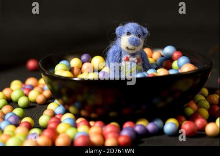 Cute blue toy bear inside a black bowl filled with colorful candies over black background Stock Photo