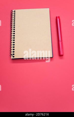 Vertical shot of a notebook and a red marker on a red surface Stock Photo