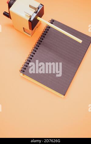 Vertical shot of a notebook and a mechanical pencil sharpener on an orange surface Stock Photo