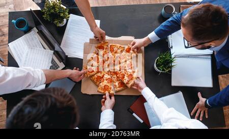 Happy diverse colleagues spend work break together eating takeaway delivery pizza in office, smiling multiracial employees have fun, laugh and chat Stock Photo
