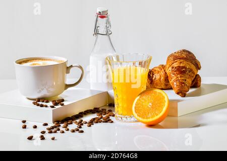 view of a delicious orange juice surrounded by coffee beans, freshly made croissants, a bottle of milk and a cup of coffee on a table. Breakfast conce Stock Photo