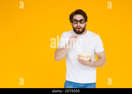 Portrait vogue young man in 3d glasses, white t-shirt watching movie film, holding popcorn, cup of soda isolated on bright yellow background. People Stock Photo