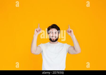 Portrait of a cheerful young man with a beard pointing his fingers in the direction of the copy space , isolated on a yellow background Stock Photo