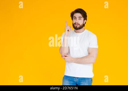 Young handsome man with beardwhite shirt standing over yellow background pointing finger up with successful idea. Exited and happy. Number one. Stock Photo