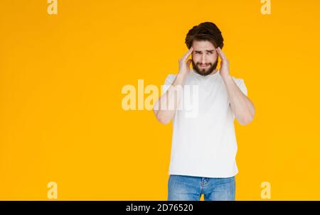 A young bearded man in a white t-shirt on a yellow background. the concept of tension , headache and fatigue Stock Photo
