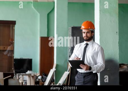 A young bearded Architect in a construction helmet on a construction site checks the result Stock Photo