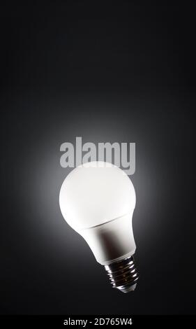 Light bulb floating in dark empty black space and shining. Power saving led light. Stock Photo