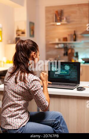 Happy woman hacker after cracking firewall of government and getting access granted. Programmer writing a dangerous malware for cyber attacks using performance laptop during midnight. Stock Photo