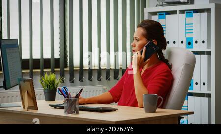Employee talking on phone in business modern office. Hispanic entrepreneur working in professional workspace, workplace in personal corporate company speaking on smartphone looking at computer desktop Stock Photo