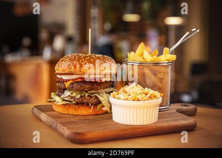 Double beef burger with cheddar and bacon served with fries and coleslaw Stock Photo