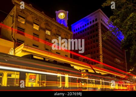 Night cityscape of downtown Long Beach's Metro train station, light trails and 1907 distinctive, historical clock tower with 6 ft diameter clock face. Stock Photo