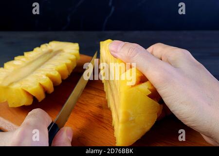 Hand cutting a peeled fresh ripe pineapple in half on a wooden board Stock Photo