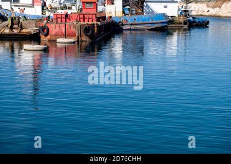 Industrial ships and boats moored in old harbor of Drapetsona Piraeus Greece, reflection on the sea water, sunny day. Stock Photo