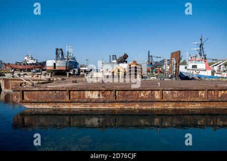 Old abandoned rusty marine platform and ships in industrial harbor of Drapetsona Piraeus Greece, blue sky and sea, sunny day. Stock Photo
