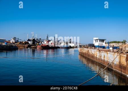 Rusty industrial ship and ships and boats moored in old harbor of Drapetsona Piraeus Greece, blue sky and sea, sunny day. Stock Photo