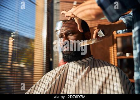Male barber combing client beard in barbershop Stock Photo