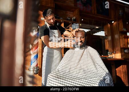Male barber shaving client beard with electric razor Stock Photo
