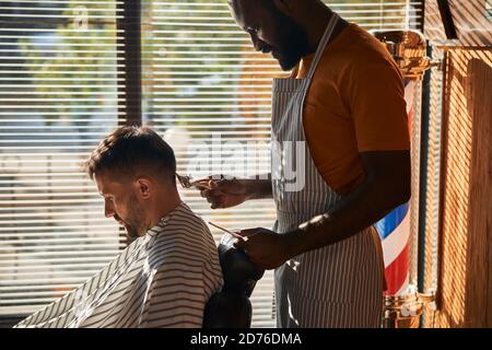 Handsome male barber cutting client hair with metal hair clipper Stock Photo