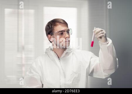 A portrait of a young scientist in protective goggles holding a test tube with a red liquid. Stock Photo