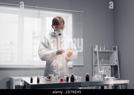 Young scientist in protective clothing and a respirator lighting up a match in his laboratory. Stock Photo