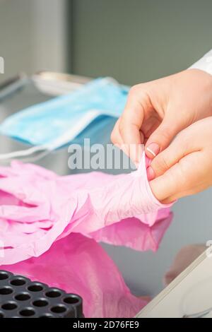 Nurse's hands putting on pink sterilized protective gloves in the laboratory Stock Photo