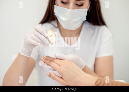 Manicure master applying warm wax from candle on fingernails of young woman in nail salon Stock Photo