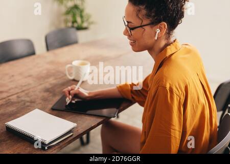 Happy business woman using stylus pen and working on a digital tablet at home. Female working from home using graphic tablet and digitized pen. Stock Photo