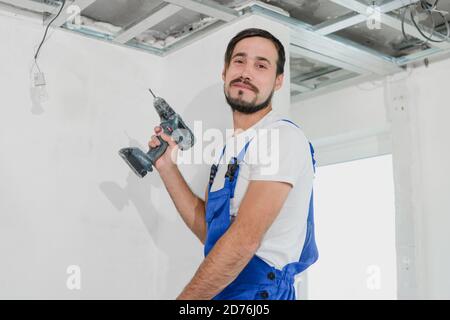The worker holds a drill in his hands. He is wearing blue overalls Stock Photo