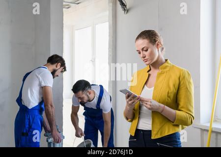 A supervisor in a jacket speaks on a cell phone. Two workers stand in the background Stock Photo