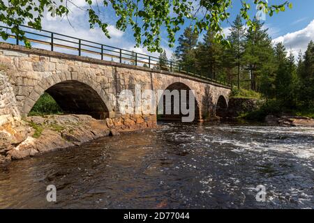 Old stone bridge over a little river in northern Sweden with a blue sky and clouds in background. Stock Photo