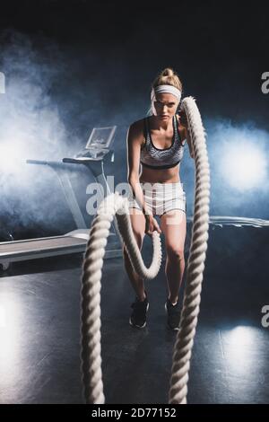 Selective focus of sportswoman exercising with battle rope in sports center with smoke Stock Photo