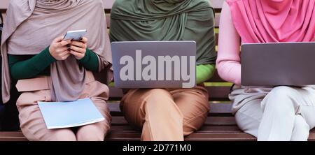Unrecognizable Arabic Women Using Phone And Laptops Learning Online Outdoors Stock Photo