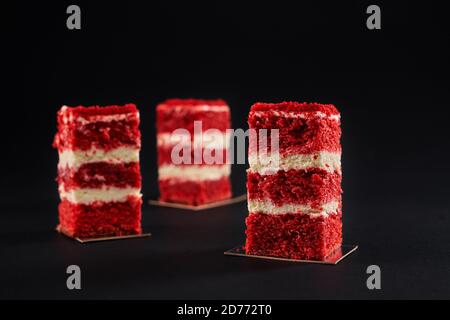 Three square slices of tasty fresh cake layered with red cherry bisсuit and white buttery cream. Closeup view of delicious homemade pastry, dessert isolated on black background Stock Photo