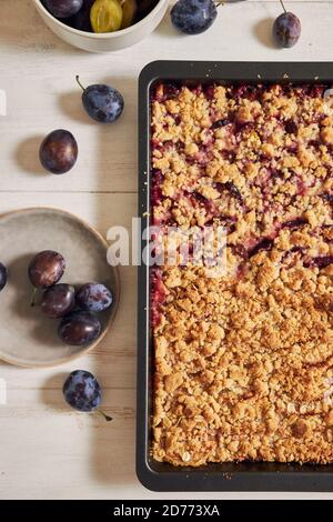 Top view of freshly baked plum cake in a pan and fresh plums on a white table Stock Photo
