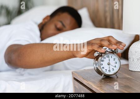 Sleepy Black Man Turning Off Alarm Clock Lying In Bed Stock Photo