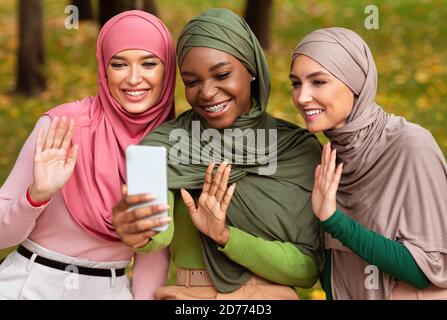 Three Modern Muslim Ladies With Smartphone Making Video Call Outside Stock Photo