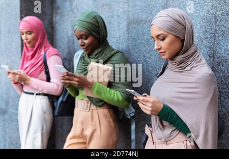 Modern Arab Ladies Using Smartphones Standing Over Gray Wall Stock Photo