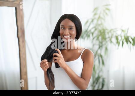 Happy african american millennial woman applying hair oil to prevent split ends Stock Photo